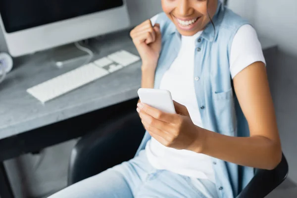 Vista cortada de Africano americano freelancer segurando smartphone e mostrando gesto de vitória, fundo borrado — Fotografia de Stock