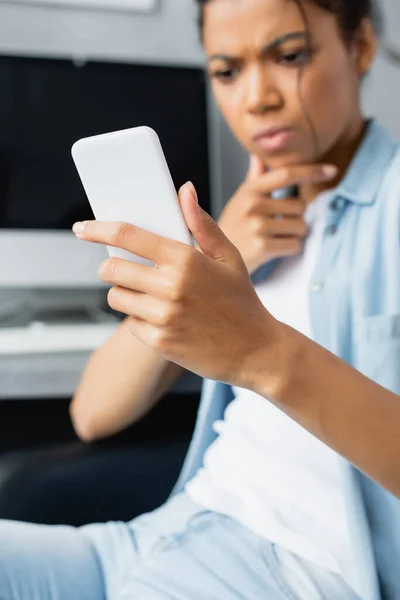 Selective focus of smartphone in hand of thoughtful african american freelancer — Stock Photo