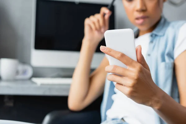 Visão parcial do freelancer americano africano segurando smartphone em casa, fundo embaçado — Fotografia de Stock