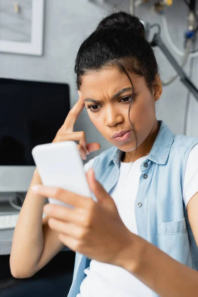 Réfléchi afro-américain pigiste tenant smartphone à la maison, flou au premier plan — Photo de stock