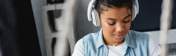 Jeune femme afro-américaine écoutant de la musique dans des écouteurs sans fil à la maison, bannière — Photo de stock