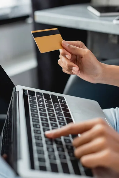 Vista parcial de la mujer afroamericana escribiendo en el ordenador portátil mientras sostiene la tarjeta de crédito, borrosa primer plano - foto de stock