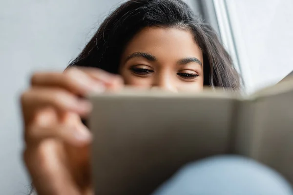 Abgeschnittene Ansicht einer afrikanisch-amerikanischen Frau, die zu Hause Buch liest, verschwommener Vordergrund — Stockfoto