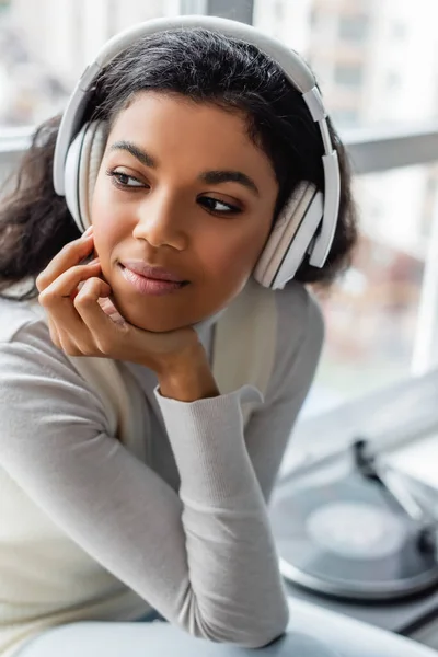 Pensive african american woman listening music in wireless headphones at home — Stock Photo