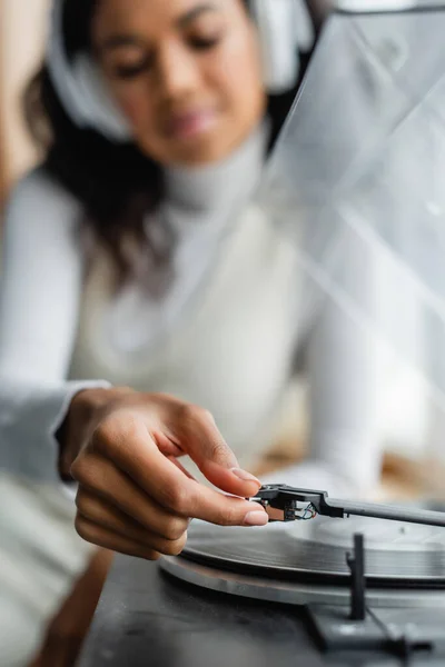 Selective focus of african american woman in wireless headphones turning on record player, blurred background — Stock Photo