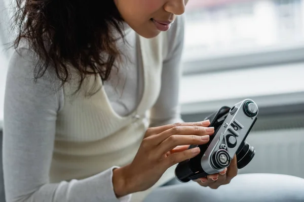 Vista recortada de la mujer afroamericana ajustando la cámara de fotos vintage en casa, fondo borroso - foto de stock