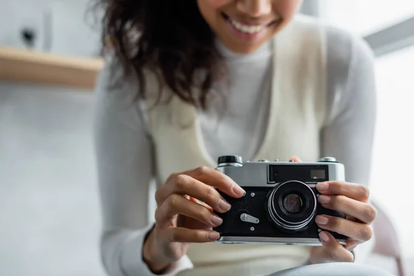 Cropped view of smiling african american woman holding vintage photo camera, blurred background — Stock Photo