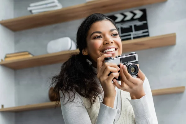 Mulher americana africana feliz sorrindo enquanto segurando câmera de fotos vintage em casa — Fotografia de Stock