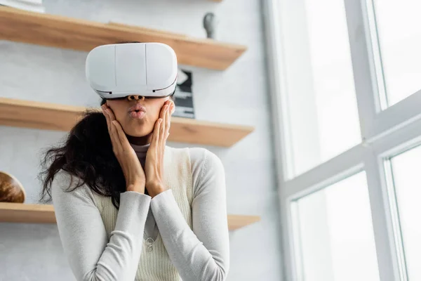 Surprised african american woman touching face and pouting lips while gaming in vr headset — Stock Photo