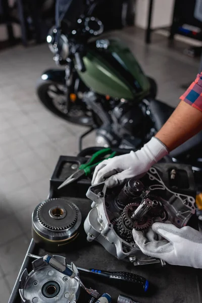 Vue recadrée du mécanicien près de la boîte de vitesses démontée et de la moto sur fond flou — Photo de stock