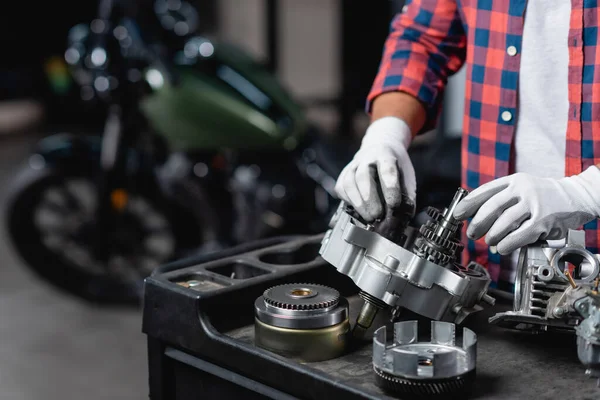 Ausgeschnittene Ansicht eines Reparateurs in Handschuhen bei der Untersuchung eines zerlegten Motorradgetriebes — Stockfoto