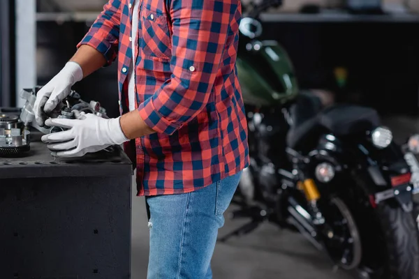 Ausgeschnittene Ansicht eines Mechanikers, der auf verschwommenem Hintergrund demontiertes Getriebe in der Nähe des Motorrads überprüft — Stock Photo