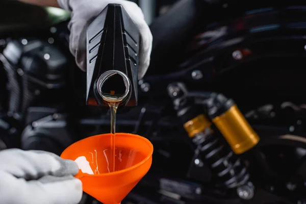 Vue partielle du mécanicien dans les gants versant l'huile moteur de la bouteille dans l'entonnoir — Photo de stock