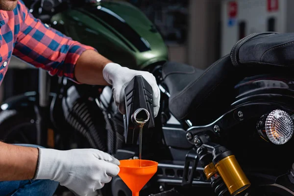 Cropped view of mechanic pouring engine oil into funnel near motorbike on blurred background — Stock Photo