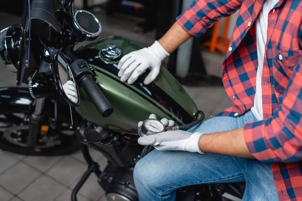 Обрізаний вид техніка в рукавичках вимірювання тиску повітря в шині мотоцикла з манометром — стокове фото