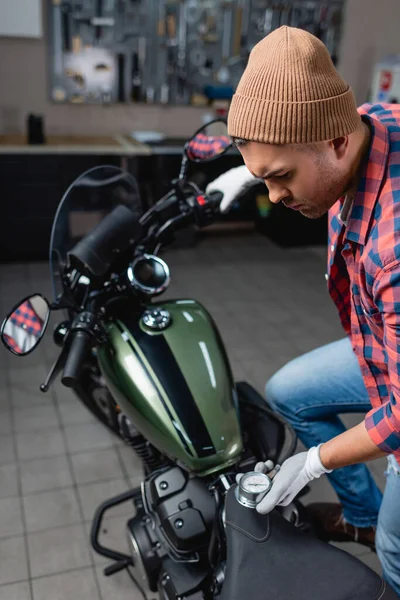 Young mechanic in beanie measuring pressure in tire of motorbike with air gauge — Stock Photo