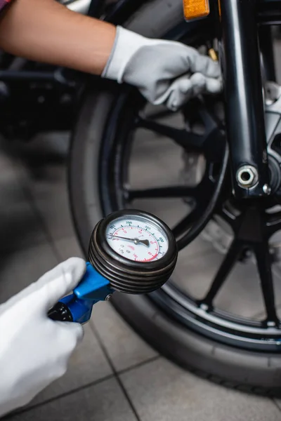 Foco selectivo del manómetro en manos de mecánico que mide la presión del aire en el neumático de la motocicleta - foto de stock
