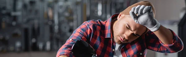 Young, tired mechanic in plaid shirt working in workshop, banner — Stock Photo