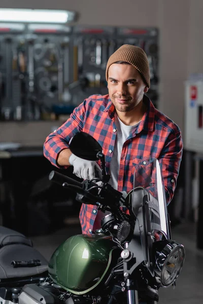 Mecánico sonriente mirando a la cámara mientras que hace el diagnóstico de la motocicleta en taller - foto de stock