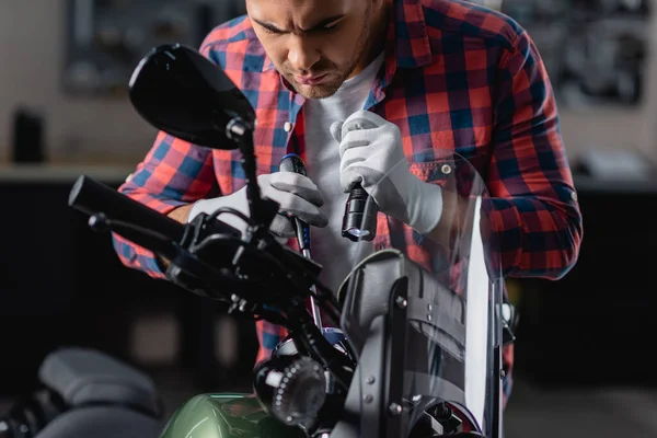 Joven reparador sosteniendo linterna y destornillador mientras comprueba moto - foto de stock