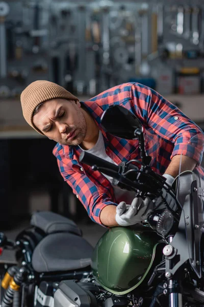 Joven mecánico en camisa a cuadros y gorro de control de manillar de la motocicleta en el taller - foto de stock