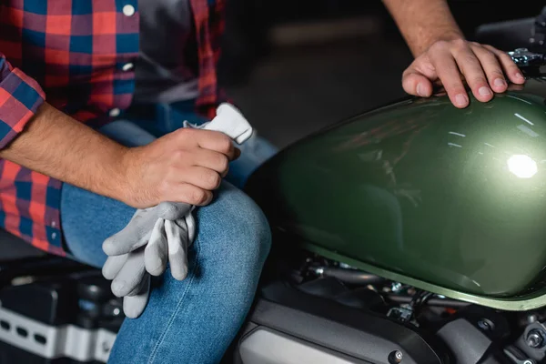 Ausgeschnittene Ansicht des Mechanikers mit Handschuhen, während er auf dem Motorrad in der Werkstatt sitzt — Stockfoto