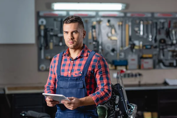 Young technician in overalls looking at camera while holding digital tablet — Stock Photo