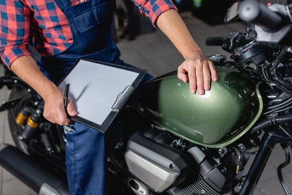 Cropped view of mechanic holding blank clipboard while sitting on motorbike in workshop — Stock Photo