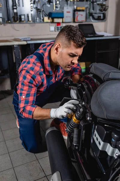 Junger Mechaniker im karierten Hemd überprüft Stoßdämpfer von Motorrad in Werkstatt — Stockfoto