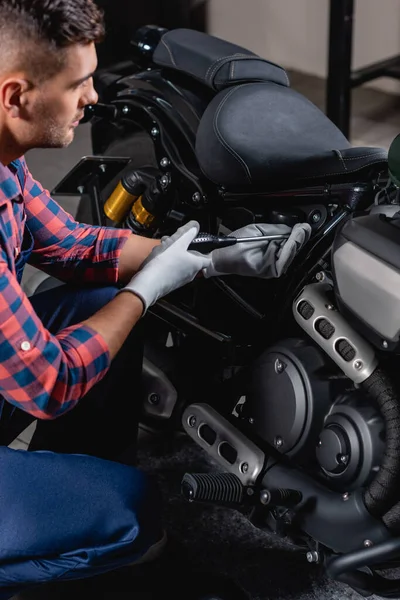 Giovane tecnico che utilizza cacciavite mentre effettua la diagnostica della moto in officina — Foto stock