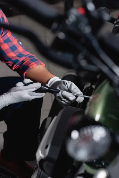 Обрезанный вид механика с помощью отвертки при проверке мотоцикла, размытый передний план — стоковое фото