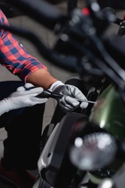 Ausgeschnittene Ansicht des Mechanikers mit Schraubenzieher bei der Kontrolle des Motorrads, verschwommener Vordergrund — Stockfoto