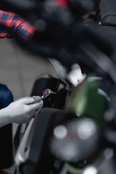 Vista recortada del técnico en guantes que sostienen la llave del zócalo cerca de la motocicleta, primer plano borroso - foto de stock