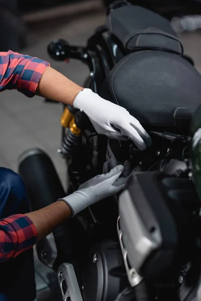 Cropped view of mechanic in gloves making diagnostics of motorbike in workshop, blurred foreground — Stock Photo