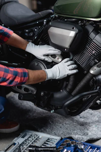 Ausgeschnittene Ansicht eines Reparateurs in Handschuhen, der Motorrad in der Nähe von Werkzeugkiste in Werkstatt überprüft — Stockfoto