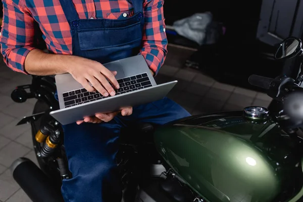 Ausgeschnittene Ansicht eines Technikers mit Laptop während er auf dem Motorrad in der Werkstatt sitzt — Stockfoto