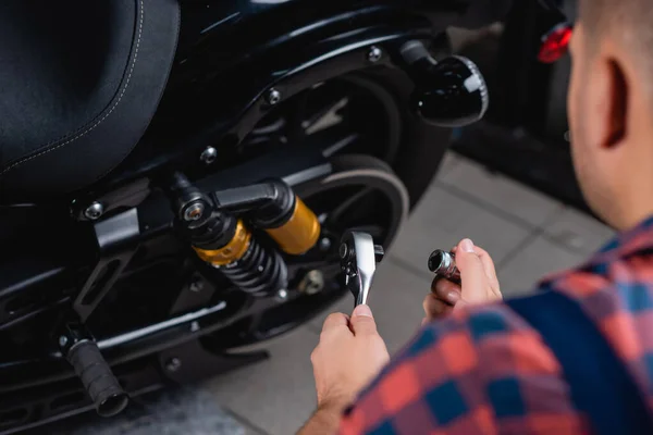 Cropped view of mechanic holding socket wrench near motorbike, blurred foreground — Stock Photo