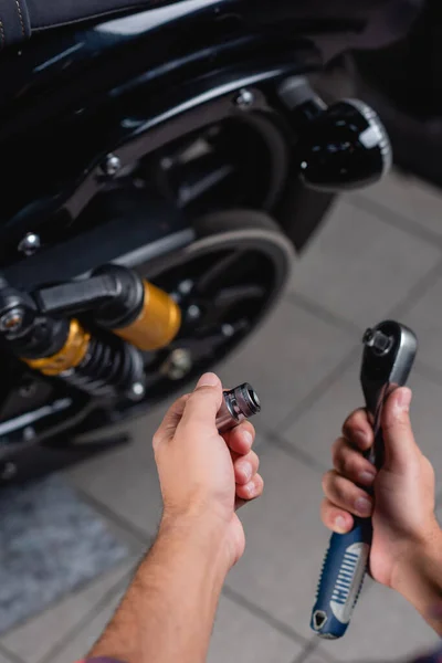 Partial view of repairman holding socket wrench near motorbike on blurred background — Stock Photo