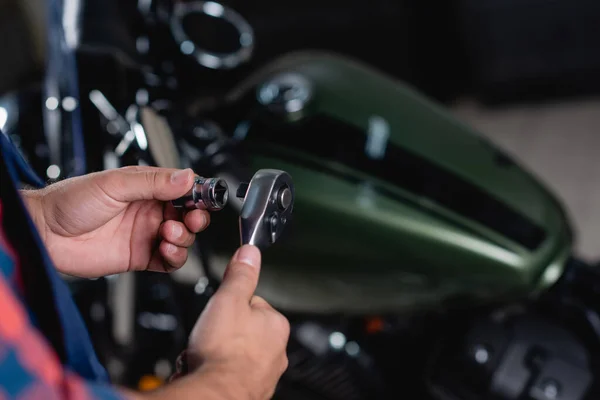 Foco selectivo de llave de zócalo en manos de mecánico cerca de la moto sobre fondo borroso - foto de stock