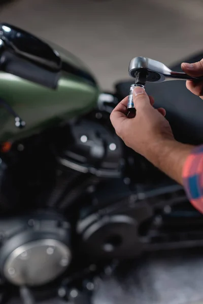 Cropped view of technician holding socket wrench near motorcycle on blurred background — Stock Photo