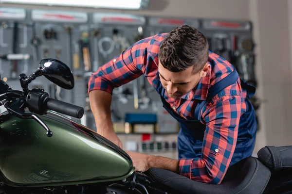 Junger Techniker im karierten Hemd begutachtet Motorrad in Werkstatt — Stockfoto