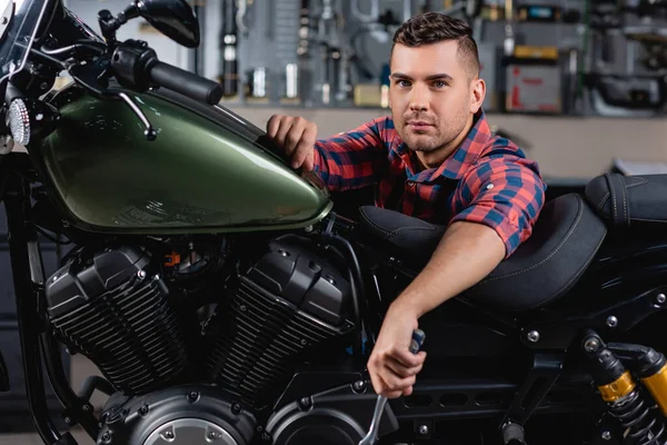 Молодий механік дивиться на камеру біля мотоцикла в майстерні — стокове фото