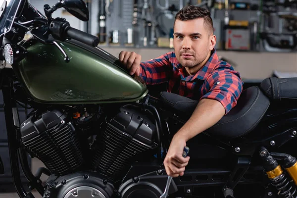 Giovane meccanico guardando la macchina fotografica vicino alla moto in officina — Stock Photo