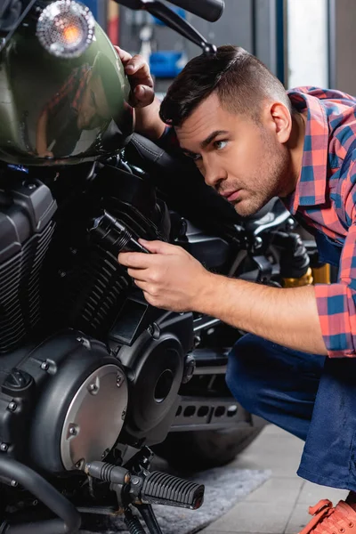Jovem mecânico segurando lanterna enquanto examina moto — Fotografia de Stock