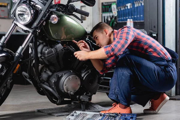 Mécanicien en salopette tenant lampe de poche tout en faisant des diagnostics de moto — Photo de stock