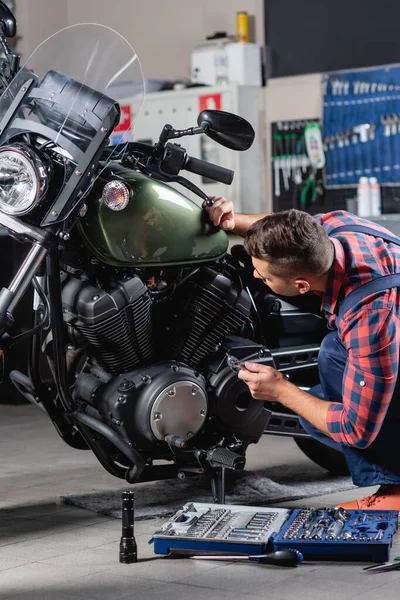 Mechanic making diagnostics of motorcycle in workshop near toolbox — Stock Photo