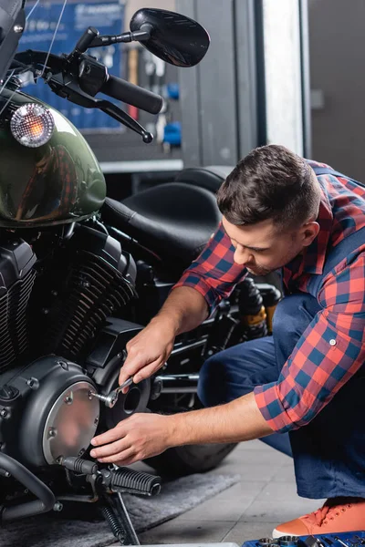 Young mechanic unscrewing cap of motorcycle gearbox with socket wrench — Stock Photo