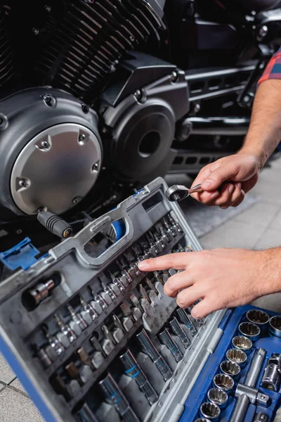 Ausgeschnittene Ansicht des Mechanikers, der mit dem Finger auf Bits für Steckschlüssel im Werkzeugkasten in der Nähe des Motorradgetriebes zeigt — Stockfoto