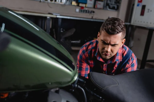 Jeune réparateur vérifiant moto en atelier au premier plan flou — Photo de stock