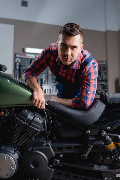 Giovane riparatore guardando la macchina fotografica mentre fa la diagnostica della moto in officina — Foto stock